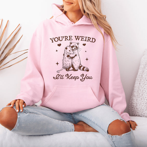 Celebrate the beauty of quirky connections with our comfy hoodie, featuring an adorable illustration of a raccoon and possum sharing a heartwarming hug.